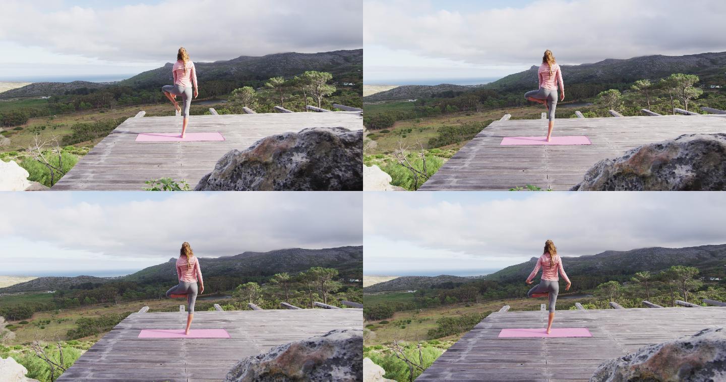 后视图的白人妇女练习瑜伽站在甲板上伸展在山坡上