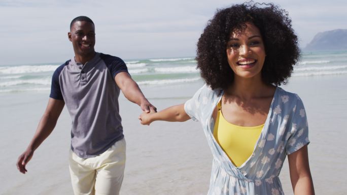 微笑的非洲裔美国夫妇在海滩上手牵手散步