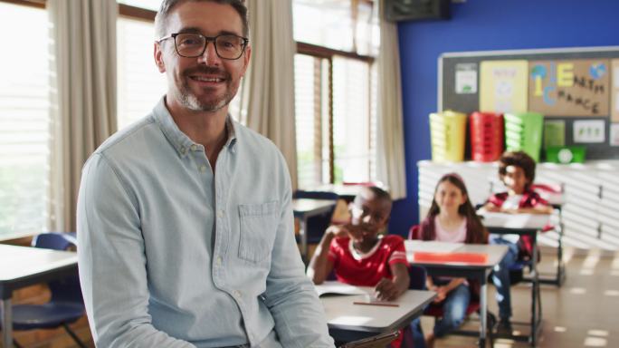 快乐的白人男教师的肖像在教室里，孩子们看着相机