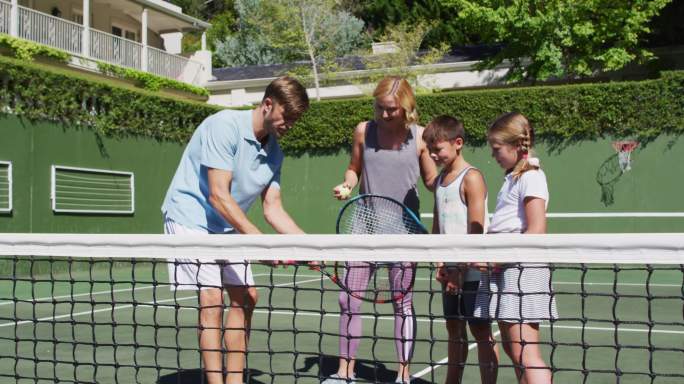 白种人的父母在一个阳光明媚的日子在网球场教他们的孩子打网球