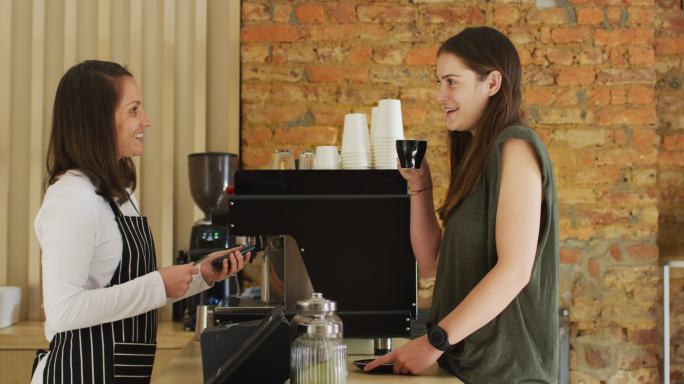 白人女服务员接受非接触式付款并将咖啡杯递给白人女顾客