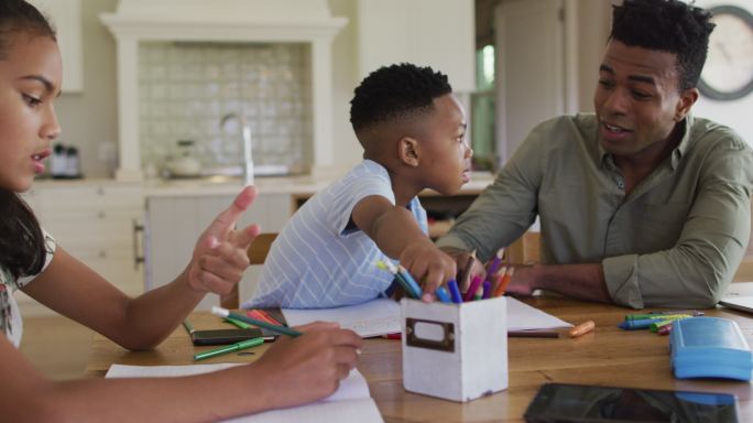 非裔美国父亲，女儿和儿子坐在厨房的桌子上做作业