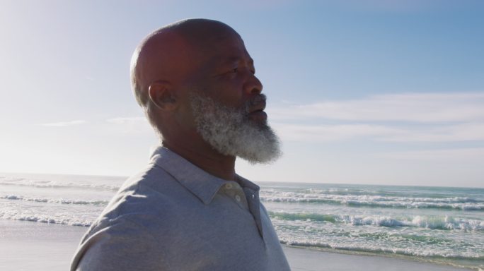 一位年长的非裔美国人站在海滩上，闭上眼睛欣赏着眼前的景色