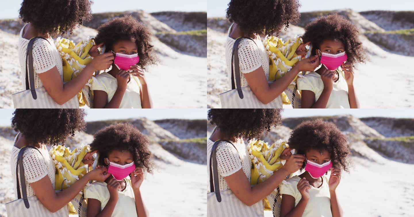 非裔美国母亲在沙滩上给女儿戴口罩