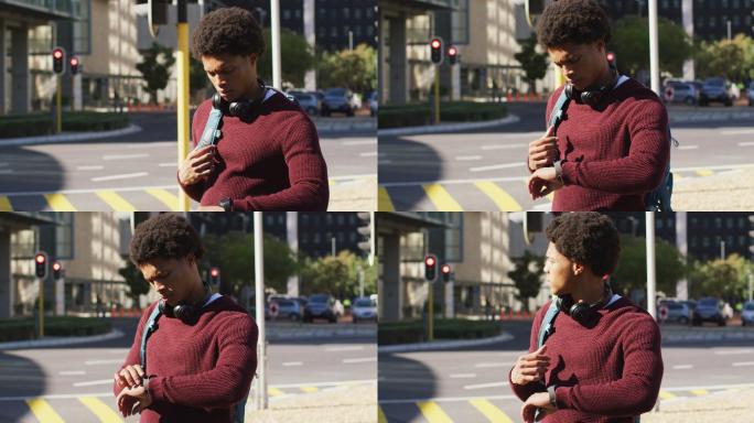 非洲裔美国人在城市中检查智能手表，戴着耳机和背包在街上等待