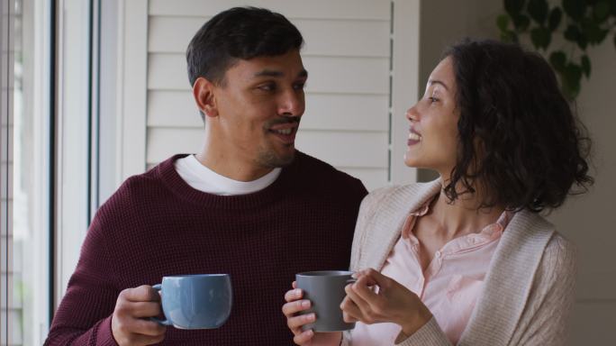 一对浪漫的西班牙夫妇站在窗前，喝着咖啡，拥抱在一起