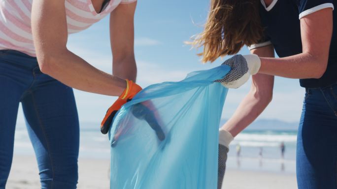 两个不同类型的女性朋友在海滩上把垃圾放进垃圾袋里
