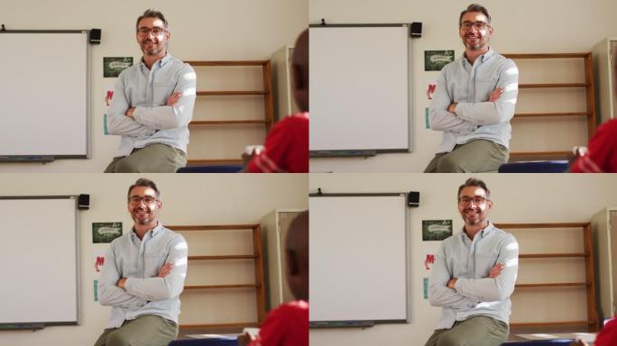 快乐的白人男性教师的肖像坐在教室的桌子上看着相机