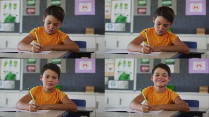 肖像快乐的混血男孩坐在教室，做笔记，看着相机