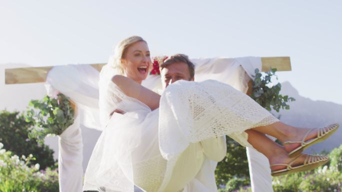 快乐的白人丈夫抱着新婚的新娘，走下户外的圣坛
