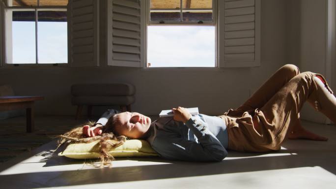 白人妇女躺在地板上拿着书，睡在阳光明媚的小屋客厅
