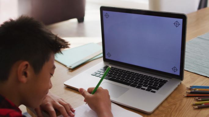 亚洲男孩在家，在网上学校课程期间使用笔记本电脑写作，在屏幕上有拷贝空间