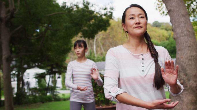 快乐的亚洲母亲与女儿在花园里锻炼，一起练习太极