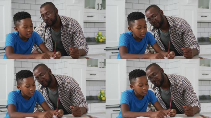 非裔美国父亲坐在餐桌旁帮助儿子做功课
