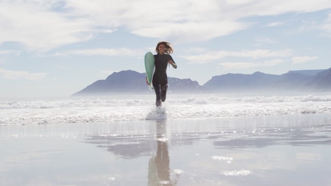 一个混血儿女人带着冲浪板从海边跑到海滩上