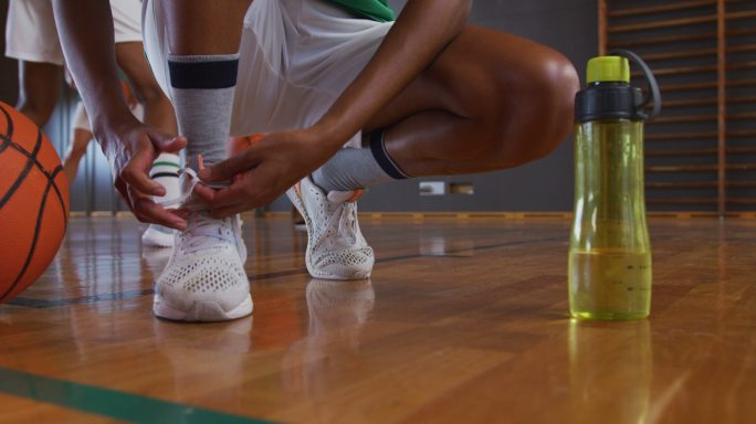 非裔美国女篮球运动员与队友在后台系鞋带