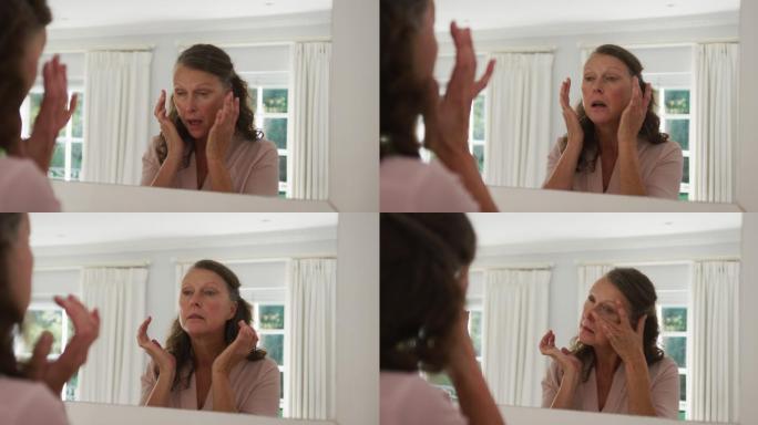 白人老年妇女站在阳光充足的房间里对着镜子检查和触摸脸部