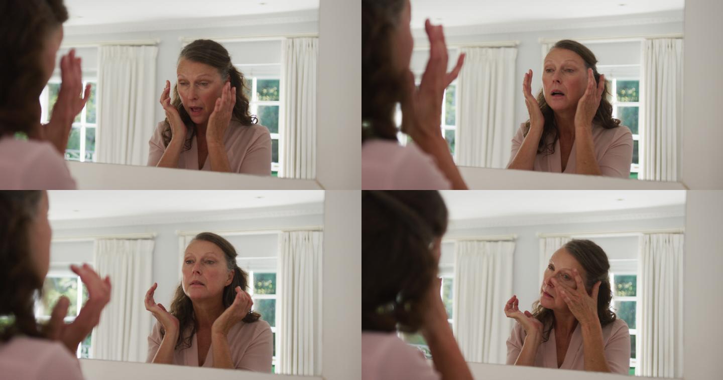 白人老年妇女站在阳光充足的房间里对着镜子检查和触摸脸部