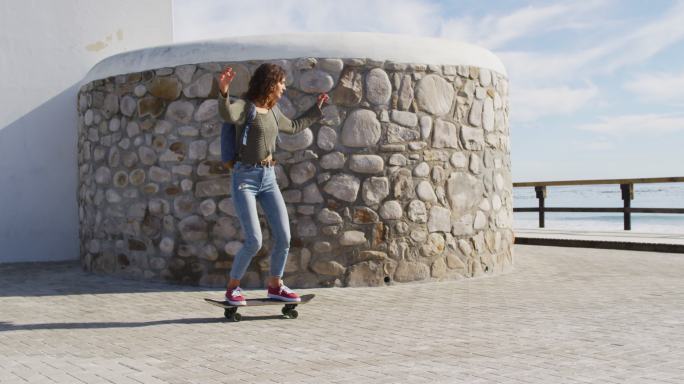 快乐的混合种族妇女滑板在阳光明媚的海滨长廊