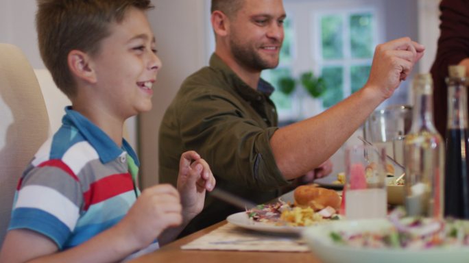 一个白人家庭在餐桌前微笑着给对方提供食物