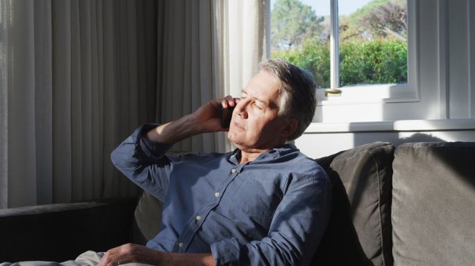 老年白人男子坐在阳光明媚的客厅通话智能手机智能手机