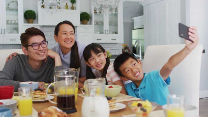 快乐的亚洲父母在厨房与儿子和女儿吃早餐，儿子在集体自拍