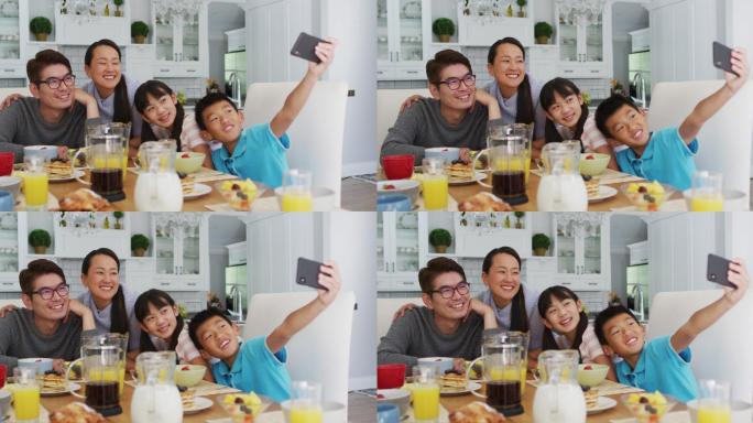 快乐的亚洲父母在厨房与儿子和女儿吃早餐，儿子在集体自拍