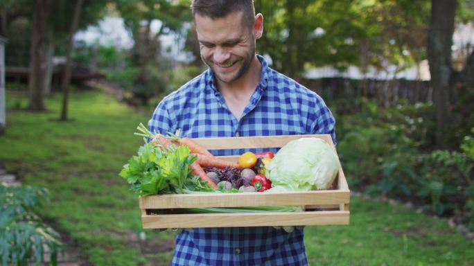 微笑的白人男子站在花园拿着一盒蔬菜