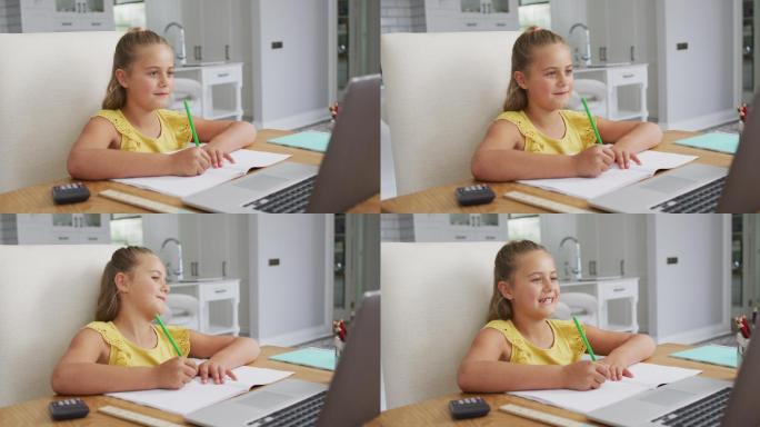 快乐的白人女孩在家里，坐在书桌上写在网上学校课程使用笔记本电脑
