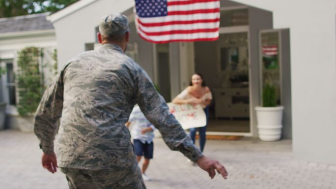 白人男性士兵在屋外打着欢迎回家的牌子，向儿子和妻子问候