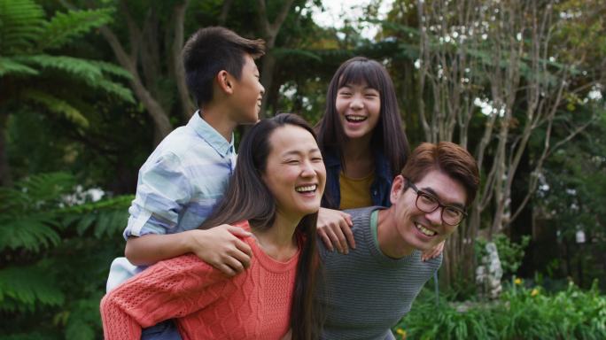 微笑的亚洲父亲和母亲猪背快乐的儿子和女儿在花园