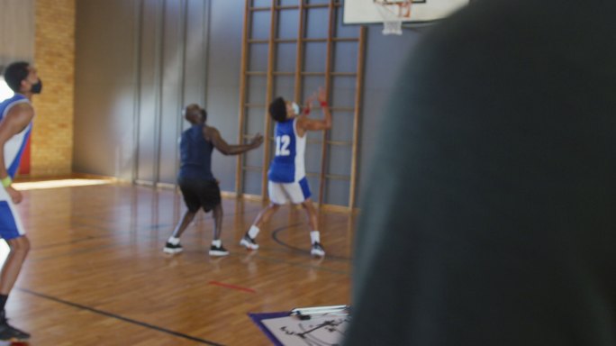 不同类型的男子篮球队在比赛中，教练拿着剪贴板，戴着口罩