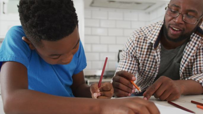 快乐的非裔美国父亲坐在餐桌旁帮助儿子做功课
