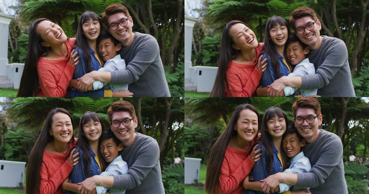 笑容满面的亚洲父母在花园里拥抱笑着的儿子和女儿