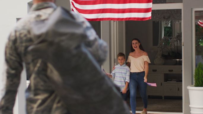 一名白人男子在花园迎接儿子和妻子，房子外面挂着美国国旗