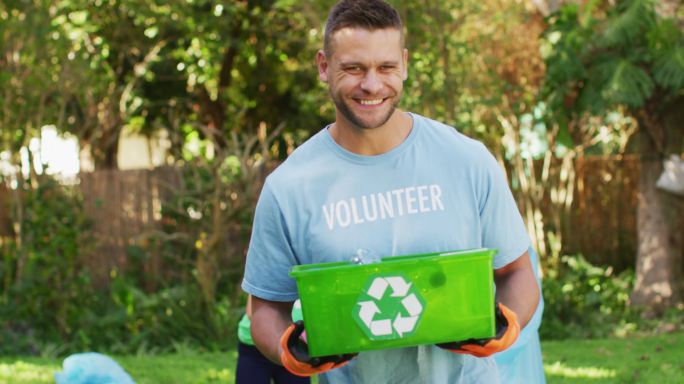 穿着志愿者t恤的白人微笑着拿着回收箱，收集塑料垃圾