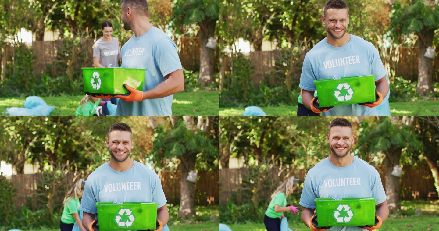 穿着志愿者t恤的白人微笑着拿着回收箱，收集塑料垃圾