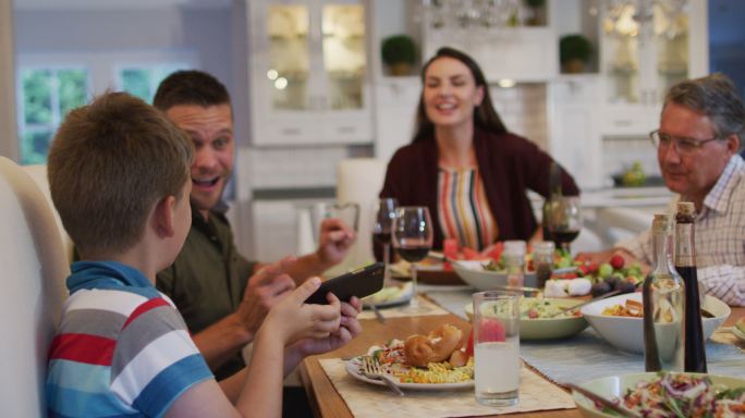 快乐的白种人孙子与父母和祖父在餐桌上自拍在家庭用餐