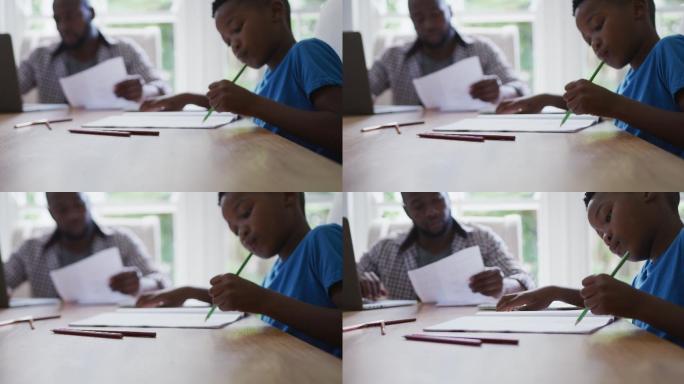 非裔美国人的儿子坐在厨房的桌子上做功课，父亲在背后工作