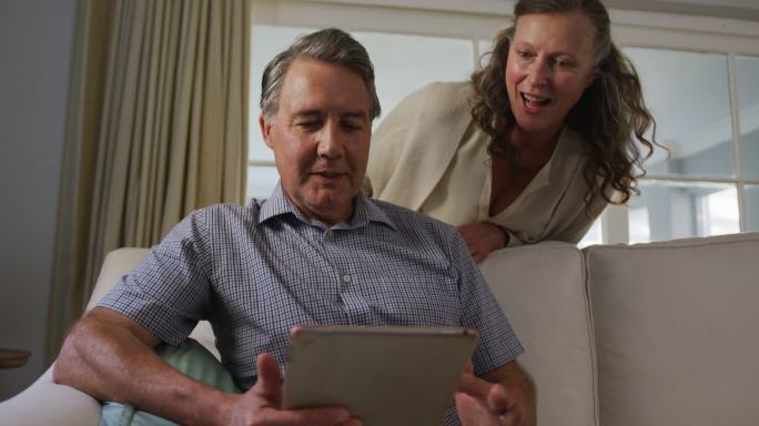 快乐的老年白人夫妇在客厅用平板电脑聊天