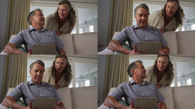 快乐的老年白人夫妇在客厅用平板电脑聊天
