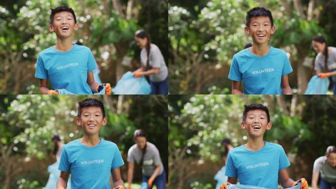 笑亚洲男孩穿着志愿者t恤拿着垃圾袋收集塑料垃圾