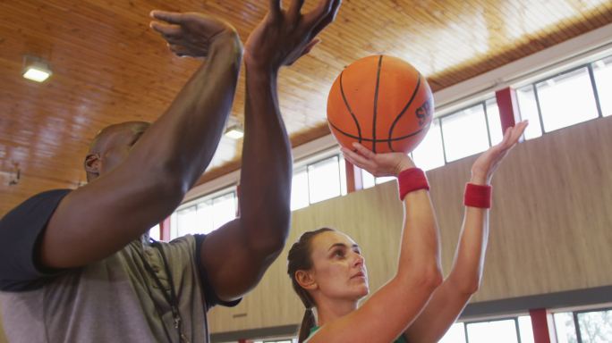 多样化的女篮球运动员和男教练练习投篮