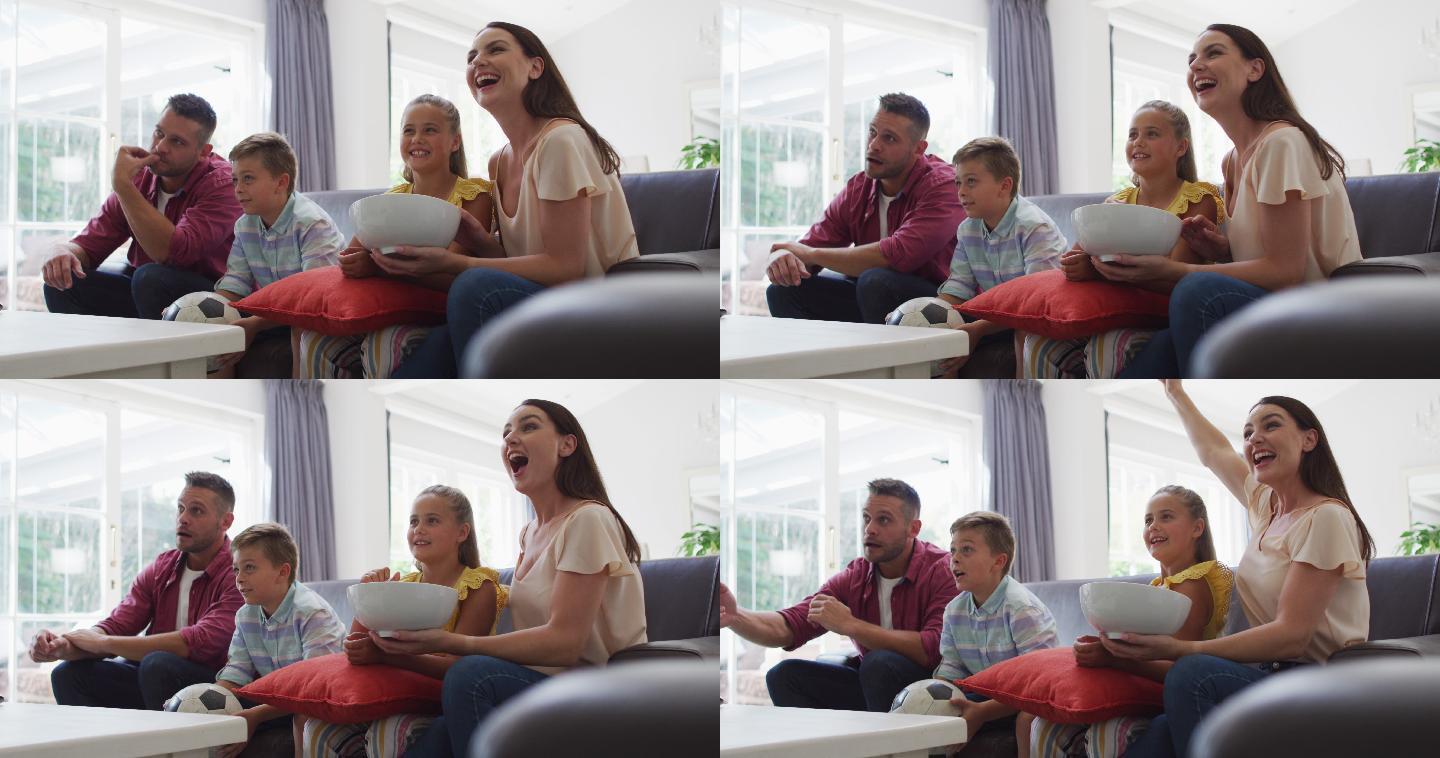 兴奋的白人父母，儿子和女儿在沙发上看电视和欢呼，儿子拿着足球