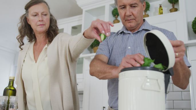 一对年长的白人夫妇在厨房准备食物，堆肥蔬菜残渣