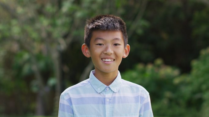 快乐的亚洲男孩的肖像看着照相机微笑和大笑在花园