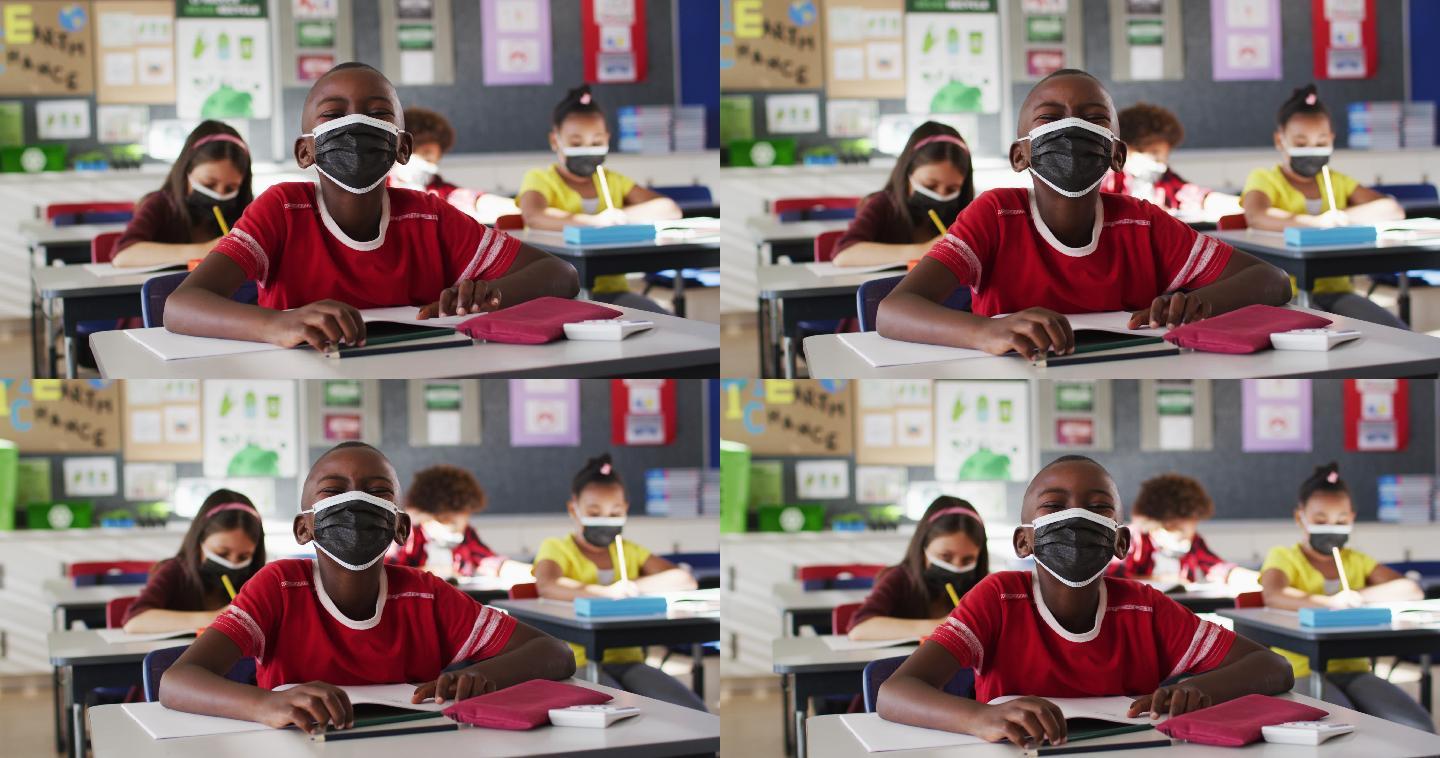 一个非裔美国男孩戴着口罩坐在学校的课桌上