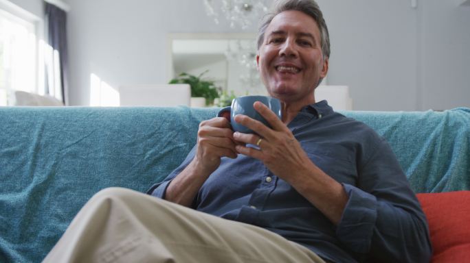 快乐的老年白人男人的肖像坐在客厅喝咖啡和微笑