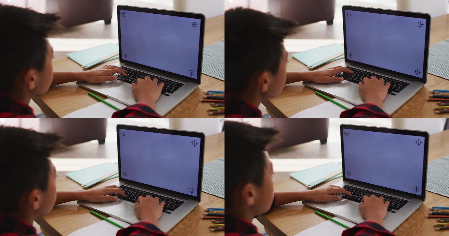 亚洲男孩在家里，坐在桌子上使用笔记本电脑在线学校课程，与复制空间在屏幕上