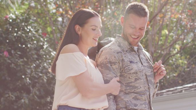 快乐的白人男性士兵提着袋子走在他微笑的妻子在花园里